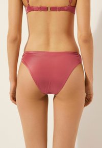 Dvoudílné fialové bikiny s hladkou, lesklou texturou. Vrchní díl má úzké ramínka a zapínání, zatímco spodní díl je s nízkým pasem a nabíranými bočními částmi.