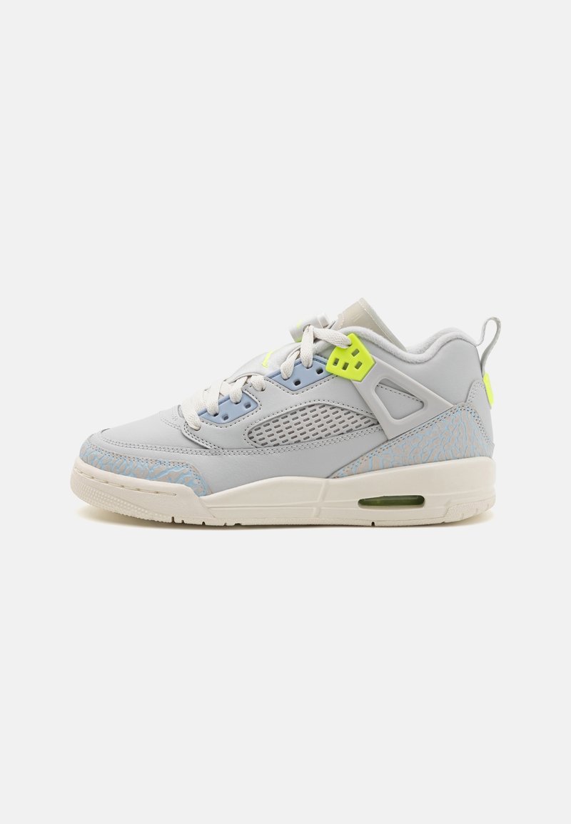 Chaussure de sport basse en gris clair avec semelle blanche, panneau en mesh, accents de lacets jaune néon et détails texturés au niveau des orteils et du talon.