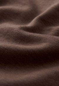 Tessuto marrone morbido con una texture fine a maglia, mostrato in primo piano con pieghe morbide e ombre.