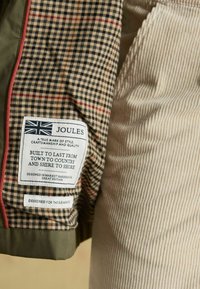 Raibumainīgs audums ar "Joules" zīmola etiķeti, kas uzsver stilu, kvalitāti un dizainu no Market Harborough, Lielbritānijā.