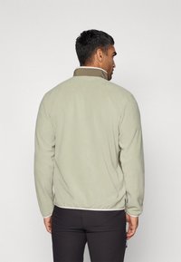 Lys grønn fleecejakke med høy krage, elastiske mansjetter og tettsittende kant. Glatt tekstur, designet for varme og komfort.