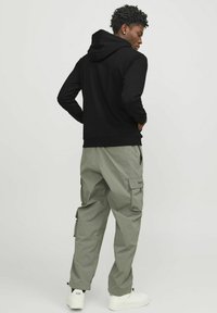 Sudadera negra con capucha combinada con pantalones cargo de color verde claro. Los pantalones cuentan con bolsillos, puños elásticos y un ajuste ligeramente relajado. Zapatillas blancas.