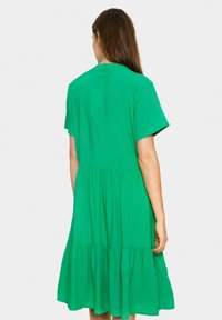 Rochie verde, cu mâneci scurte, din material moale, având un tiv în straturi cu o formă fluidă și o croială lejera. Fără modele vizibile sau accente.