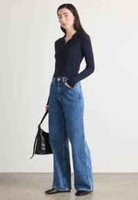 Jūras spēku zili riboti zip-up tops, kas apvienots ar augsto vidukli zilām platām džinsa biksēm, papildināts ar melnu somu un melnām norādītām kurpēm.