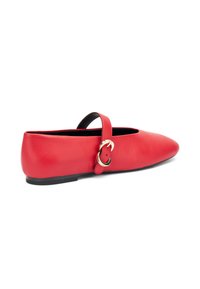 Zapato plano de piel roja con punta puntiaguda, correa para el tobillo y detalles en metal dorado. Presenta una textura suave y una suela negra baja.