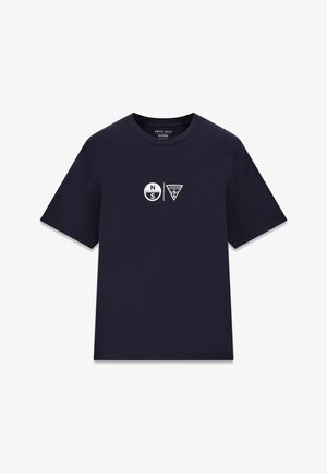 T-shirt bleu marine à manches courtes avec col rond et logos blancs North Sails et Guess centrés sur la poitrine.