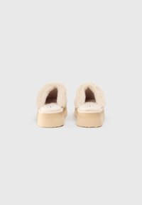 Beige åpne tøfler med en myk, behagelig overdel og teksturert brun såle, som har et lavt plattformdesign.