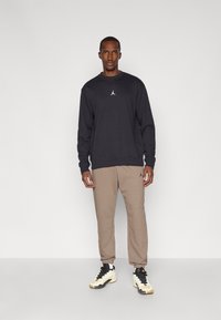 Schwarzer Crew-Neck-Sweatshirt mit kleinem Logo, sandfarbene tapered Sweatpants und schwarz-weiße Sneaker. Glattes Material, lockere Passform, lässiges Design.