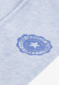 Svijetloplava pamučna tkanina s kružnim plavim logotipom na kojem se nalazi tekst i zvijezda, nalik na vintage brand emblem.