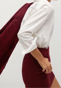 Camicia bianca a colletto abbinata a una mini gonna testurizzata bordeaux e un cappotto coordinato, caratterizzati da un motivo a chevron e un design aderente.