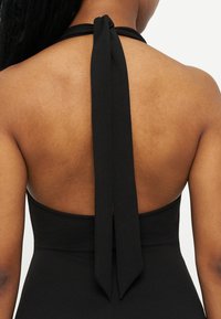 Πλάγια όψη μιας γυναίκας που φοράει μαύρο τοπ με halter και δεμένη φιόγκο στο πίσω μέρος του λαιμού της, με εκτεθειμένη την άνω πλάτη.