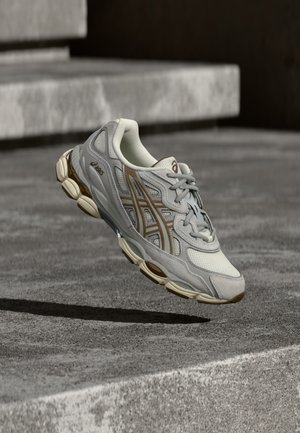 Jasnoszare buty do biegania z siateczkową cholewką i brązowymi akcentami, charakteryzujące się amortyzowaną podeszwą i teksturowaną gumową podeszwą zewnętrzną.