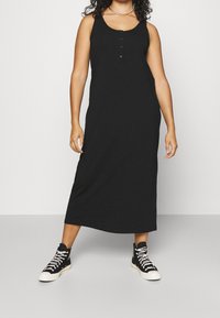 Schwarzes, ärmelloses Maxikleid mit rundem Ausschnitt, Frontknöpfen und relaxtem Schnitt, kombiniert mit schwarzen High-Top-Sneakern.