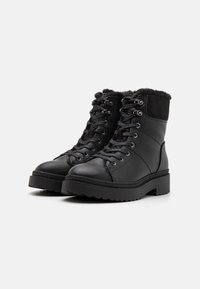 Black ankle boots made of leather with a suede panel, featuring a faux fur collar, round toe, lace-up front, and textured sole.
