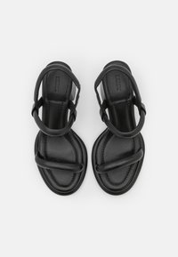 Svarta lädersandaler med platt sula, minimalistisch remdesign och en slät yta, sedda uppifrån.