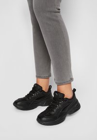 Scarpe da atletica nere realizzate in materiali mesh e sintetici, con linguetta imbottita e lacci, abbinate a jeans cropped grigi.