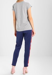 Camiseta gris de manga corta con puños enrollados, combinada con joggers azul marino que presentan franjas laterales rojas y rosas y un diseño elegante y ajustado.