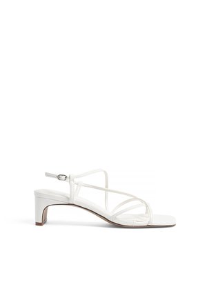 Sandales à talons blancs avec un design de lanières croisées, bout ouvert et un seducis élégant à petit talon. Matériau synthétique lisse et style minimaliste.