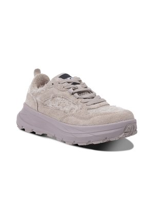 Jasnobeżowy sneaker z grubą podeszwą, cholewka z zamszu i teksturowanej tkaniny, sznurowadła oraz pętelka z tyłu, pokazany pod kątem w prawo na białym tle.