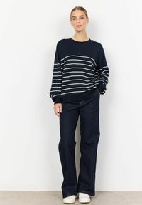 Navy sweatshirt with white horizontal stripes, crew neckline, relaxed fit, paired with dark denim flared pants and white sneakers.