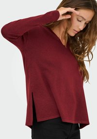 Maglione bordeaux a maniche lunghe con scollatura a V e spacco laterale; texture morbida e vestibilità rilassata, che mette in risalto un design sobrio.