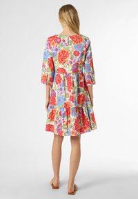 Floral cotton dress with three-quarter sleeves, tiered skirt, vibrant red, blue, and green patterns, round neck, and back keyhole detail.