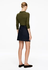 Olive ribbed long-sleeve top paired with a dark denim A-line skirt. The skirt features a simple hem and is worn with dark slip-on shoes.
