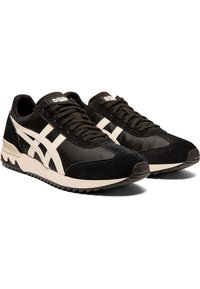 Black athletic shoes made of suede and synthetic materials, featuring a cream stripe design, sturdy rubber sole, and lace-up closure.