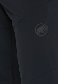 Gros plan d’un tissu foncé avec des coutures discrètes et un petit logo mammouth embossé dans un cercle.