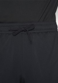 Zwarte sportshorts van een gestructureerde, ademende meshstof. Beschikt over een verstelbare tailleband en kleine perforaties voor ventilatie.