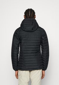 Mustapufferitakki, jossa on vaakasuora tikkipinta, huppu ja kevyt rakenne. Takapuolet näyttää tiukan istuvuuden ja sileän rakenteen.