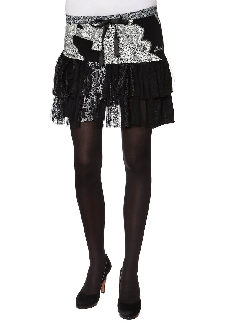 Jupe en dentelle noire à volants avec patchwork en dentelle blanche et ceinture en tissu à nouer, portée avec des collants noirs transparents et des talons hauts noirs.