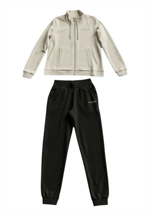 Giacca beige con zip, coulisse e due tasche laterali, abbinata a pantaloni jogger neri con polsini elasticizzati, entrambi con il marchio "FREDDY".