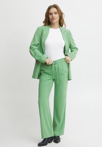 Green blazer with matching pants featuring an elastic waistband. Plain white t-shirt underneath. Black heeled boots complete the look.