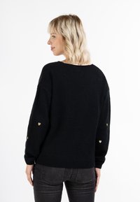 Pulover negru cu o croială lejeră, decorat cu accente de inimă aurie pe manșete și un tiv cu model în bucle. Textură moale și decolteu rotund.