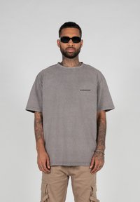 Gray oversized t-shirt with short sleeves, crew neck, and subtle brand logo on the chest. Worn with light-colored cargo pants.