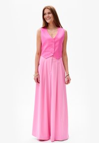 Ensemble rose en deux pièces comprenant un gilet sans manches à boutons et une jupe longue et fluide, tous deux en tissu lisse.