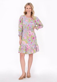 Rochie florală cu un fundal bleu deschis, având flori roz și verzi, mâneci trei sferturi, talie elastică și tiv franjurat. Tocuri pătrate maro.