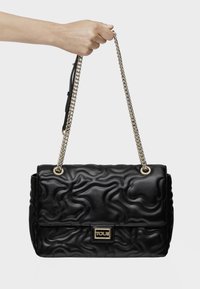 Borsa a tracolla in pelle trapuntata nera con hardware dorato, una catena come manico e una placca con logo. Presenta un design testurizzato a onde sulla superficie.