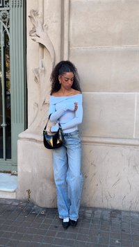 Top bleu deschis cu umerii goi și textură rib, jeans din denim deschis cu croială lejeră, geantă neagră lucioasă și pantofi negri cu toc ascuțit. Culoare solidă cu textură minimă.