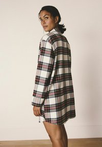 Plaid flanelinė marškinė balta, raudona, mėlyna ir žalia spalvomis; laisvas kirpimas; kišenė krūtinėje; ilgomis rankovėmis; su sagutėmis; vidutinio ilgio iki šlaunų.