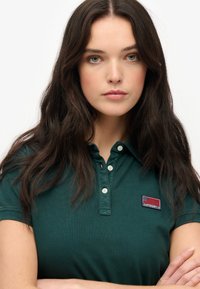 Groene polo met een gemêleerde afwerking, drie-knopen sluiting en een geborduurd logo patch met een vlag ontwerp. Van katoen.