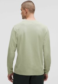 Langärmliges Shirt aus leichtem grünen Baumwollstoff, mit rundem Ausschnitt, lockerer Passform und gestickten Details an den Ärmeln und am Saum.