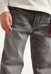 Grå denim jeans med en let falmet finish, der har et traditionelt fem-lomme-design og synlige sømme langs sømmene.