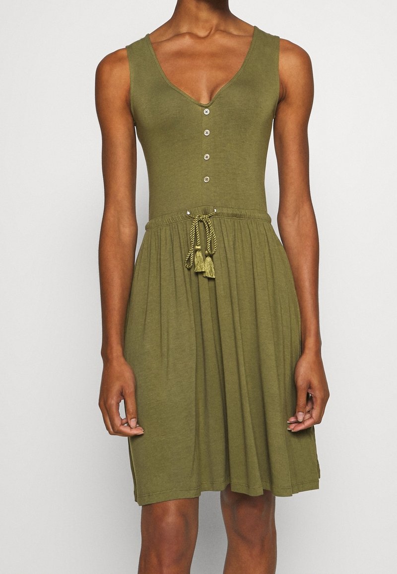 Robe sans manches vert olive avec col en V, quatre boutons sur le corsage et une taille à cordon avec des pompons.