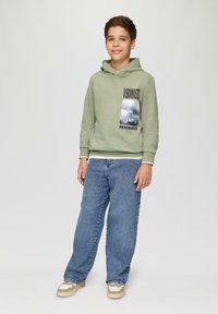 Capuchon sweatshirt in lichtgroen met graphic print, gecombineerd met losse blauwe jeans en beige sneakers met witte accenten.