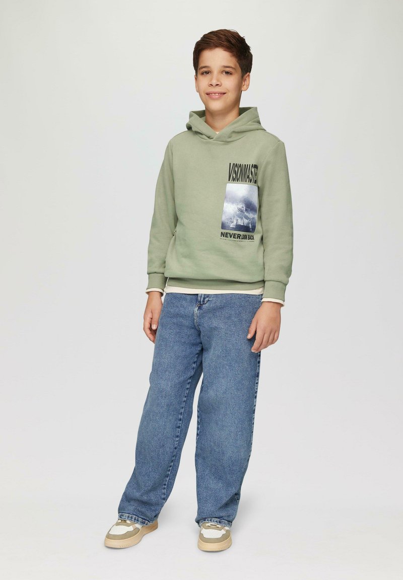 Capuchon sweatshirt in lichtgroen met graphic print, gecombineerd met losse blauwe jeans en beige sneakers met witte accenten.