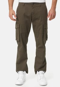 Cargo pants in olive green, made of cotton, featuring multiple side pockets, a relaxed fit, and visible stitching details. Paired with white sneakers.