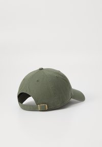 Casquette de baseball en coton vert olive avec une visière incurvée, une sangle réglable et un détail en métal doré à l'arrière. Tissu texturé.