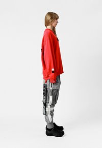 Sudadera roja, pantalones cargo gris con correas y etiquetas, y calzado negro. Un ajuste casual con una silueta relajada y materiales texturizados.
